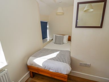 A small bedroom with a single bed a checked pillow and blanket a wall-mounted mirror and a window with a blind at Little Cowarne Court in Little Cowarne near Bromyard