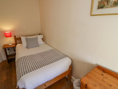 A small bedroom with a single bed white bedding checkered pillow and blanket a wooden side table with a red lamp and a wooden dresser at Little Cowarne Court in Little Cowarne near Bromyard