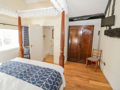 A bedroom with a four-poster bed blue and white bedding wooden wardrobe chair and a wall-mounted TV at Little Cowarne Court Little Cowarne near Bromyard