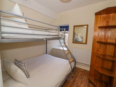A small bedroom with metal bunk beds a wooden corner shelf a wall mirror and a window at Little Cowarne Court in Little Cowarne near Bromyard