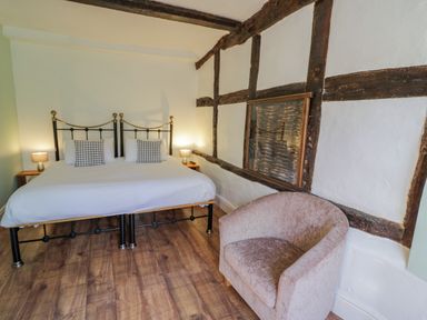 A bedroom with a double bed two bedside lamps an armchair and exposed wooden beams on the walls at Little Cowarne Court in Little Cowarne near Bromyard