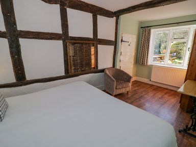 A bedroom with a bed a chair a window and exposed wooden beams at Little Cowarne Court in Little Cowarne near Bromyard