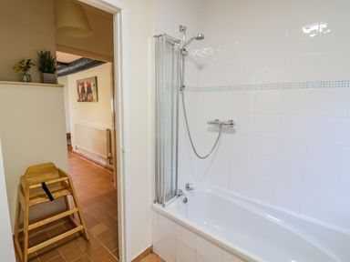 A bathroom with a bathtub and shower next to a wooden high chair at Little Cowarne Court in Little Cowarne near Bromyard