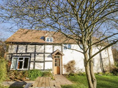 A cottage with timber frame details and a wooden door with a tree in the front garden at Little Cowarne Court in Little Cowarne near Bromyard