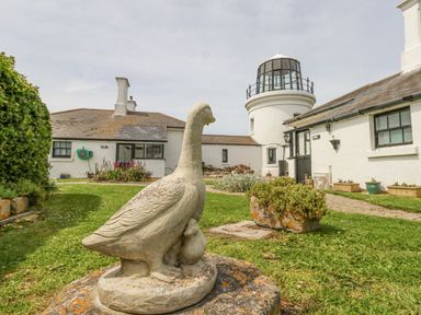 Stone goose sculpture on grass with white buildings and a lighthouse tower in the background at Old Higher Lighthouse Stopes Cottage in Portland Bill