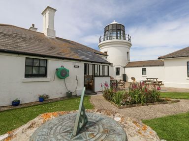 An outdoor courtyard with a sundial flower bed and a lighthouse in the background at Old Higher Lighthouse Stopes Cottage Portland Bill