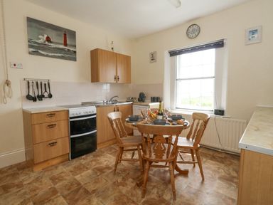 A kitchen with wooden cabinets a stove a dining table with four chairs and a large window at Old Higher Lighthouse Stopes Cottage Portland Bill