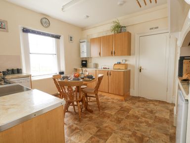 A kitchen with wooden cabinets a round table with chairs and tableware a window and a door at Old Higher Lighthouse Stopes Cottage Portland Bill