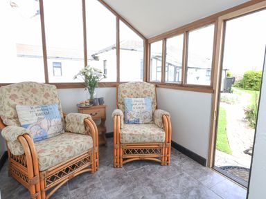 A small sunroom with two armchairs and a side table with flowers and mugs at Old Higher Lighthouse Stopes Cottage Portland Bill