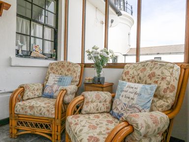A seating area with two floral armchairs and a small wooden table with flowers and cups by windows showing part of a lighthouse at Old Higher Lighthouse Stopes Cottage Portland Bill
