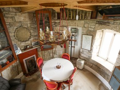 A small dining area with a round table and red chairs in a stone-walled room at Old Higher Lighthouse Stopes Cottage Portland Bill