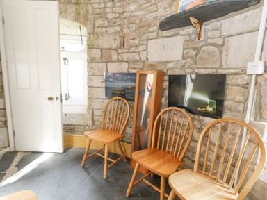 A stone wall room with three wooden chairs a white door and photographs on the wall at Old Higher Lighthouse Stopes Cottage Portland Bill