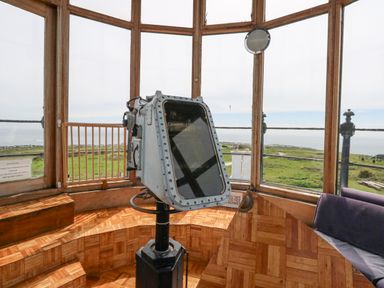 Inside a lighthouse with a mounted metal telescope and wooden flooring at Old Higher Lighthouse Stopes Cottage in Portland Bill