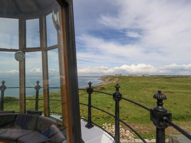 View from inside a lighthouse with railing outside overlooking green fields cliffs and the ocean at Old Higher Lighthouse Stopes Cottage Portland Bill
