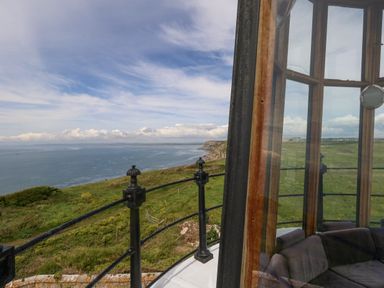 A coastal landscape with grassy cliffs and ocean viewed from a lighthouse balcony at Old Higher Lighthouse Stopes Cottage Portland Bill