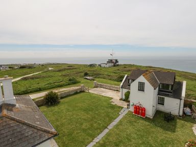A coastal view with a white house and grassy area near the ocean at Old Higher Lighthouse Stopes Cottage Portland Bill
