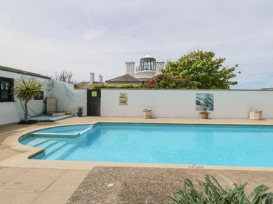 An outdoor swimming pool with a white wall surrounding it and a lighthouse visible in the background at Old Higher Lighthouse Stopes Cottage in Portland Bill