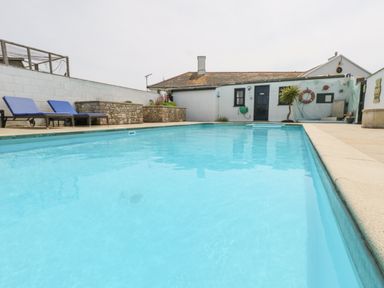 An outdoor swimming pool with two blue lounge chairs and a small building in the background at Old Higher Lighthouse Stopes Cottage Portland Bill