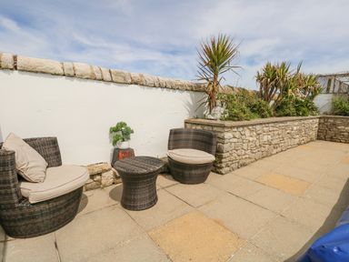 An outdoor patio with two wicker chairs and a table beside a stone wall with plants at Old Higher Lighthouse Stopes Cottage Portland Bill