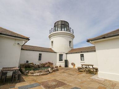 A courtyard with a lighthouse tower a stone pond wooden tables and benches at Old Higher Lighthouse Stopes Cottage Portland Bill