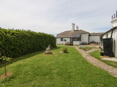 A garden with a stone duck statue and pathways leading to a white house at Old Higher Lighthouse Stopes Cottage in Portland Bill