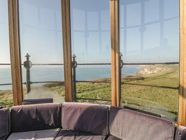 A corner seating area with windows overlooking a grassy cliff and ocean at Old Higher Lighthouse Branscombe Lodge Portland Bill