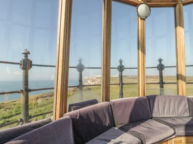 A curved seating area inside a glass enclosure with a view of the coastline and grassy cliffs at Old Higher Lighthouse Branscombe Lodge Portland Bill