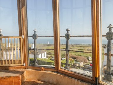 A room with large windows overlooking a coastal landscape with houses and grass at Old Higher Lighthouse Branscombe Lodge Portland Bill