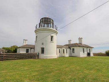 A white lighthouse building with an attached house and green lawn at Old Higher Lighthouse Branscombe Lodge Portland Bill