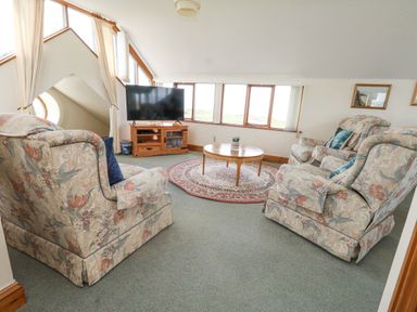 A living room with floral armchairs a round coffee table a television on a wooden stand and windows at Old Higher Lighthouse Branscombe Lodge Portland Bill