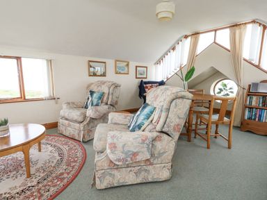 A sitting area with two floral armchairs a round wooden table and a dining table with chairs near windows at Old Higher Lighthouse Branscombe Lodge Portland Bill