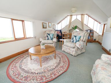 A sitting room with armchairs a round wooden table a patterned rug and windows at Old Higher Lighthouse Branscombe Lodge Portland Bill