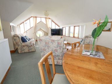 A living room with floral armchairs a wooden round dining table a flat screen tv and multiple windows at Old Higher Lighthouse Branscombe Lodge Portland Bill