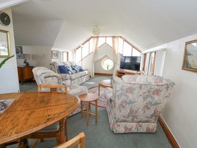 A living room with patterned sofas a wooden dining table a television and a round window at Old Higher Lighthouse Branscombe Lodge Portland Bill