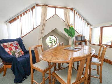 A dining area with a round wooden table and chairs near triangular windows with vertical blinds at Old Higher Lighthouse Branscombe Lodge Portland Bill