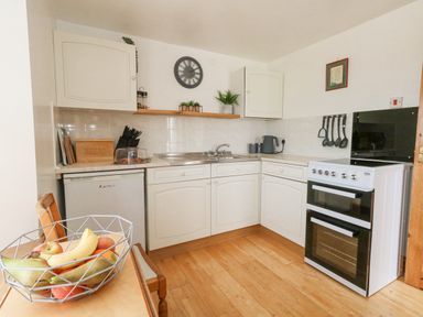 A kitchen with white cabinets a stove a sink a fridge and a bowl of fruit on a table at Old Higher Lighthouse Branscombe Lodge Portland Bill