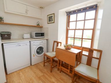 A small kitchen area with a dishwasher washing machine wooden table chairs and a window at Old Higher Lighthouse Branscombe Lodge Portland Bill