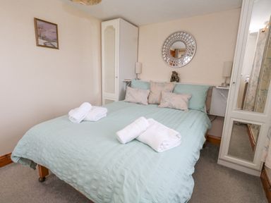 A bedroom with a bed with blue bedding towels pillows bedside lamps a wardrobe and a decorative mirror at Old Higher Lighthouse Branscombe Lodge Portland Bill