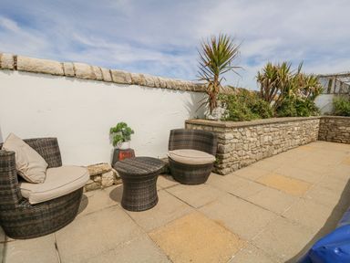 An outdoor patio with wicker chairs and a table next to a stone wall with plants at Old Higher Lighthouse Branscombe Lodge Portland Bill