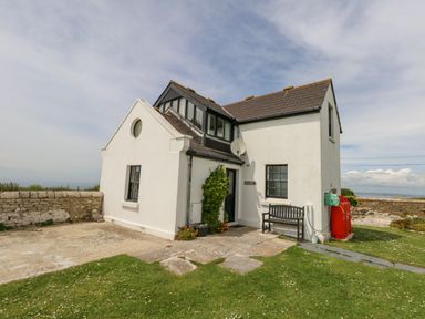 A white two-story house with black roof tiles a bench near the door and a stone wall in a grassy yard at Old Higher Lighthouse Branscombe Lodge Portland Bill