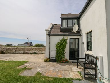 The exterior of a white house with a black bench near the door and stone paving in the yard at Old Higher Lighthouse Branscombe Lodge Portland Bill