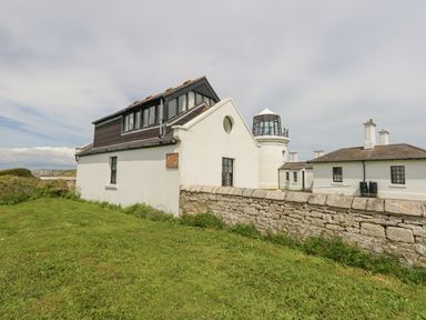 A white building with a lighthouse tower and stone wall on a grassy area at Old Higher Lighthouse Branscombe Lodge in Portland Bill