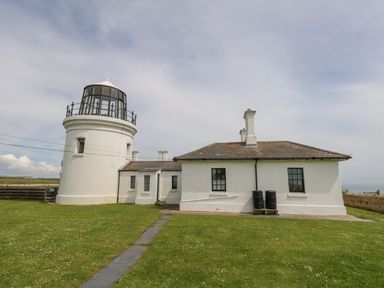 A white lighthouse with attached building on a grassy area at Old Higher Lighthouse Branscombe Lodge Portland Bill