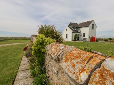 A stone wall with plants and flowers beside a white house with a pitched roof at Old Higher Lighthouse Branscombe Lodge Portland Bill