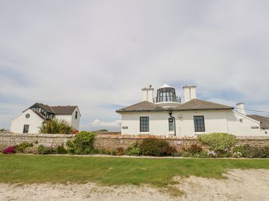 A white building with a glass lantern room and stone wall with plants at Old Higher Lighthouse Branscombe Lodge Portland Bill
