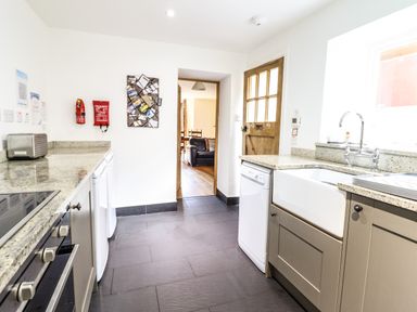 A kitchen with a toaster, dishwasher, sink, oven, and granite countertops at 3 Railway Cottages in Betws-y-Coed