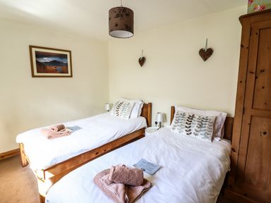 A bedroom with two single beds wooden furniture and folded towels at 3 Railway Cottages in Betws-y-Coed