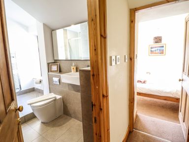 A bathroom with a toilet and sink next to a hallway leading to a bedroom with a bed and framed picture at 3 Railway Cottages in Betws-y-Coed