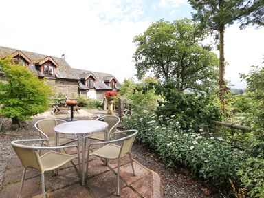 An outdoor patio area with a table and four chairs surrounded by trees and flowers at Cedar Cottage in Llanidloes