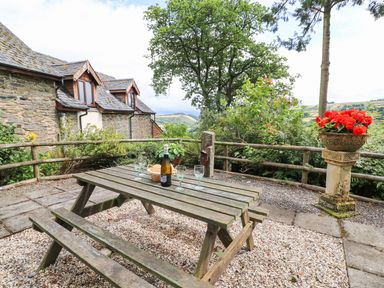 An outdoor picnic table with glasses and a bottle near a stone building and flowers at Cedar Cottage in Llanidloes